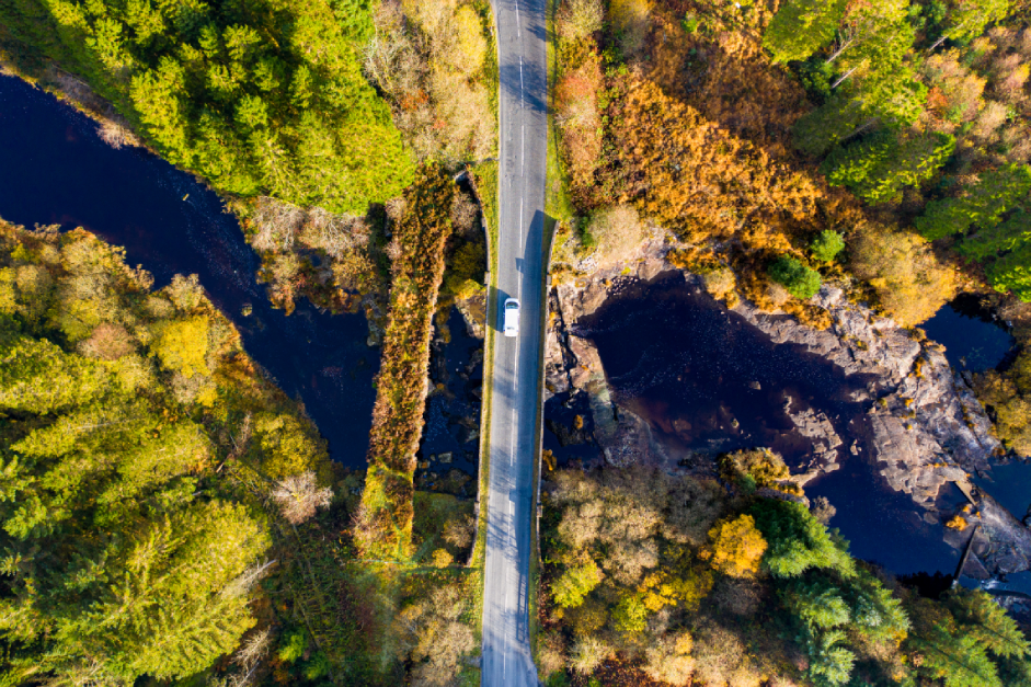 Aerial shot of car driving over a rural bridge in Scotland and into the horizon.